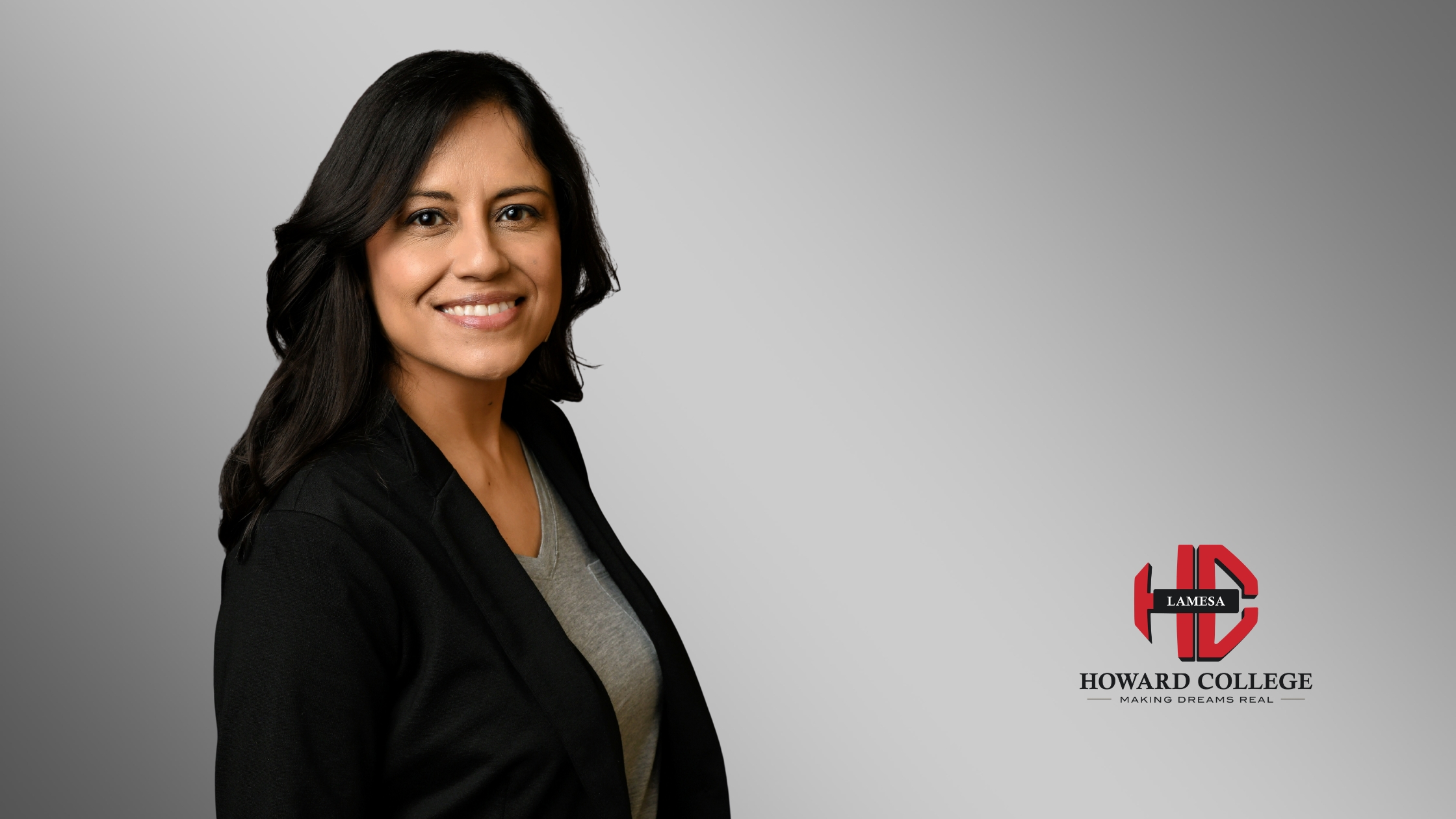 Portrait of a smiling woman with long dark hair, wearing a black top, posed in front of a gray background with the Howard College Lamesa logo.