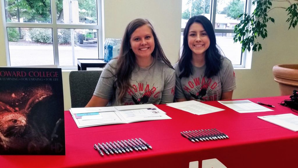 Image of two smiling women sitting behind red table