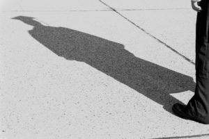 Greyscale image of shadow on sidewalk of person dressed in graduation cap and gown