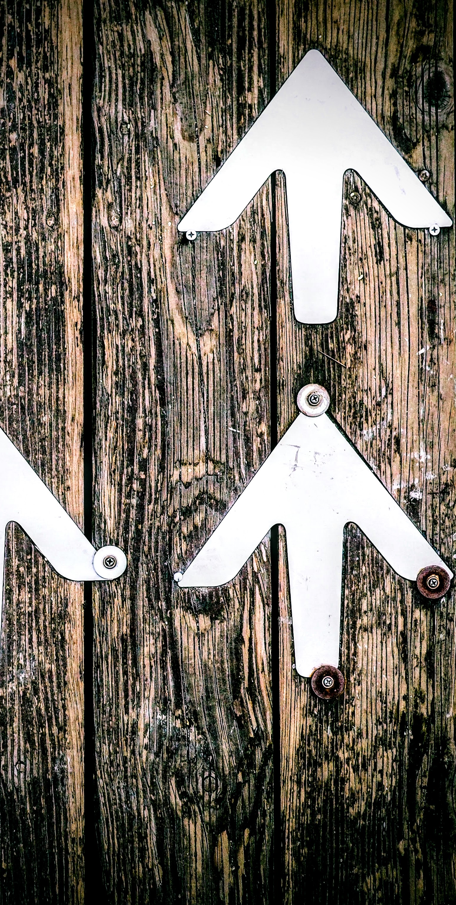 Image of textured wooden planks with white, metal arrows pointed upwards, screwed onto wood